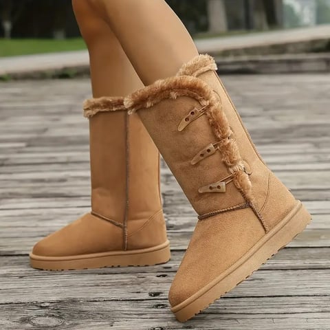 Woman wearing tan suede winter boots with fur trim standing on wooden deck outdoors